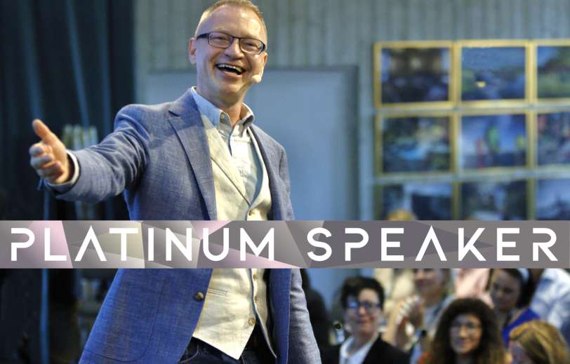 Föreläsare Tomas Eriksson på scen med stort leende och armen utsträckt - Platinum Speaker